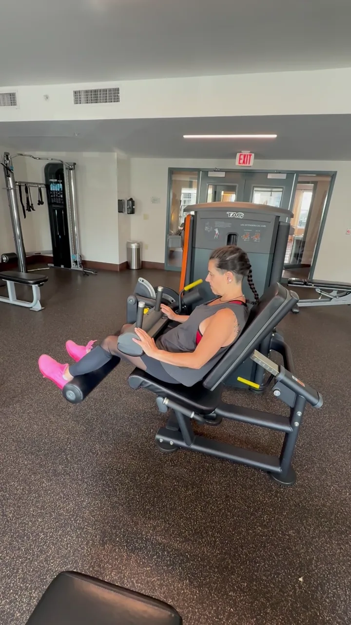 Client on a leg-extension machine in a small fitness room during a 1-on-1 session