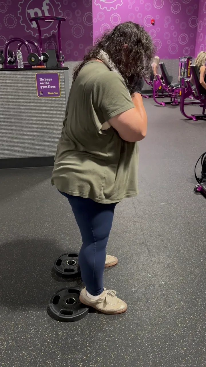 Client setting up for a squat with weight plates at her feet in a commercial gym